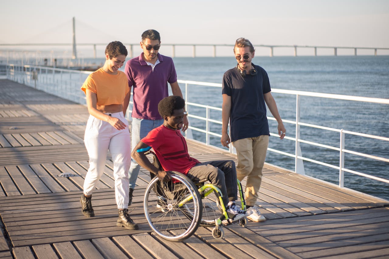 A diverse group of friends, including one in a wheelchair, enjoying a sunny stroll on a boardwalk in Portugal.