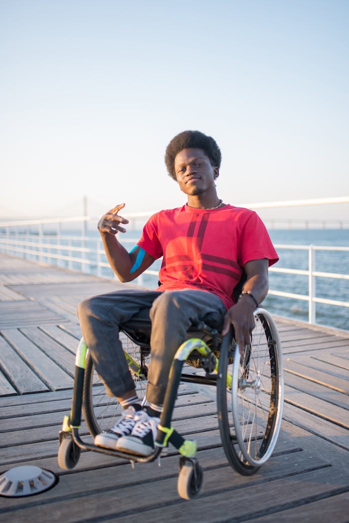 African American man in a wheelchair on a sunny boardwalk in Portugal, wearing a red shirt.